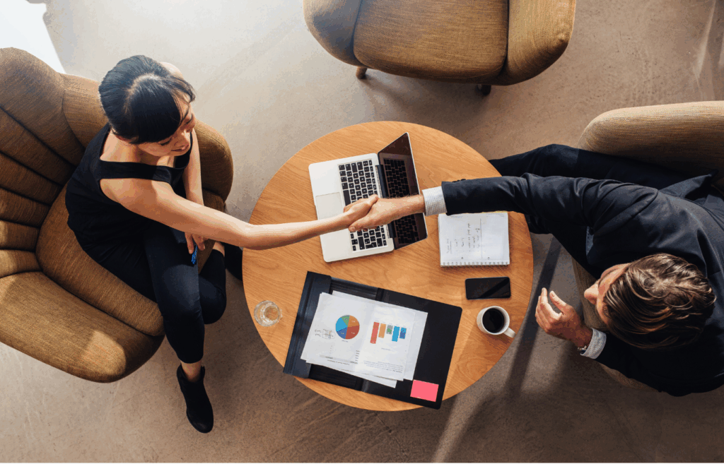 Contact image about 2 partners entering a deal above a coffee table holding a laptop, a notebook and papers